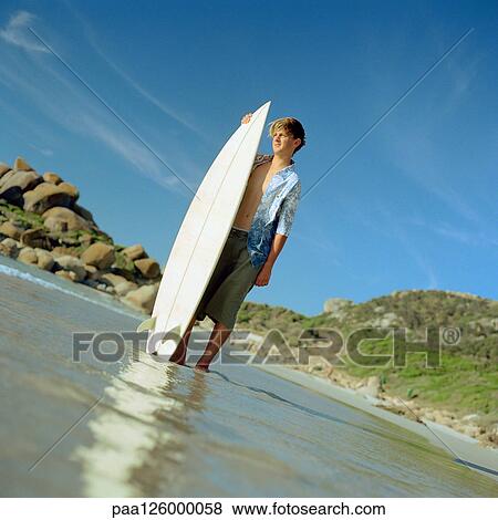 Boy standing in shallow water with surfboard View Large Photo Image Stock Photo - Boy standing in shallow water with surfboard. Fotosearch