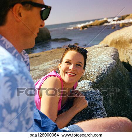 Couple resting on rock in front of sea View Large Photo Image Picture - Couple resting on rock in front of sea. Fotosearch