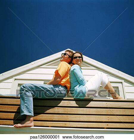 Stock Image - Couple sitting back to back, outside. Fotosearch
