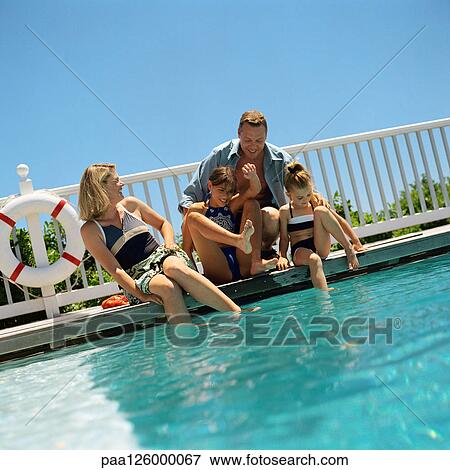 Stock Photo - Family sitting at edge of swimming pool. Fotosearch