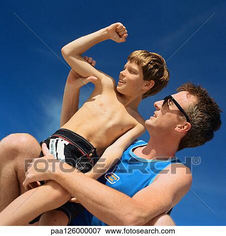Stock Photo - Father holding son, boy flexing arm, low angle view. Fotosearch