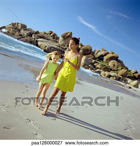 Girl and little sister holding hands while walking on beach View Large Photo Image Stock Photo - Girl and little sister holding hands while walking on beach. Fotosearch