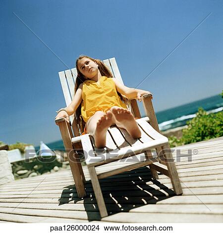 Girl sitting in deckchair, sea in background View Large Photo Image Picture - Girl sitting in deckchair, sea in background. Fotosearch