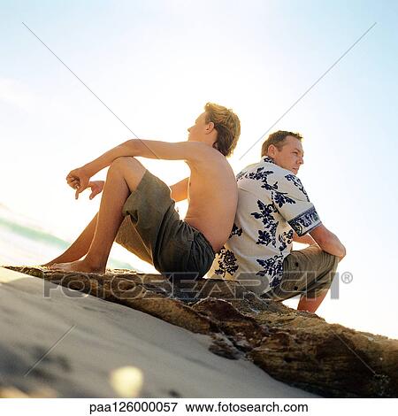 Stock Photo - Man and boy sitting back to back on beach. Fotosearch