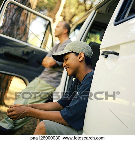 Stock Image - Man and teenage boy waiting at van with open doors. Fotosearch