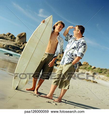 Man standing next to boy with surfboard on beach View Large Photo Image Stock Photo - Man standing next to boy with surfboard on beach. Fotosearch