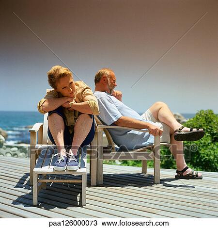 Stock Image - Mature couple sitting in deckchairs outside. Fotosearch