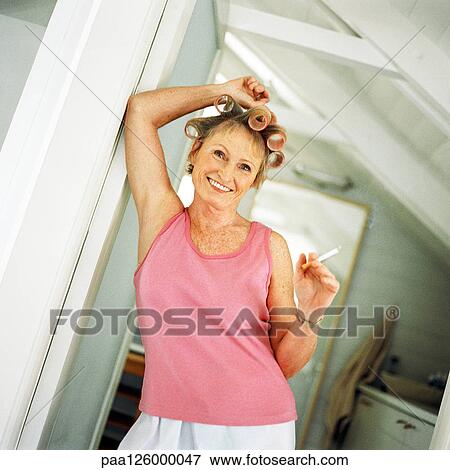 Stock Photo - Mature woman with rollers in hair holding cigarette. Fotosearch