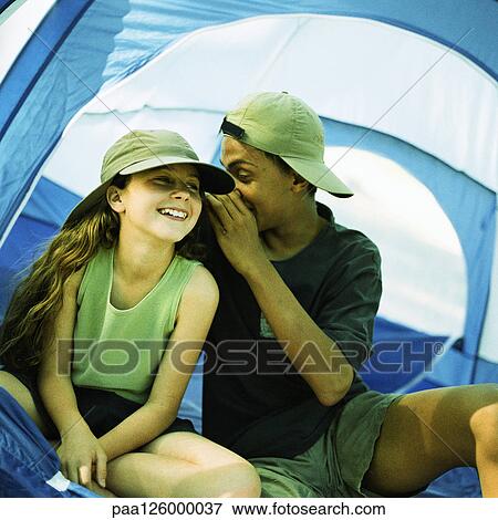 Stock Photo - Teenage boy and little girl sitting tent, boy whispering to girl. Fotosearch