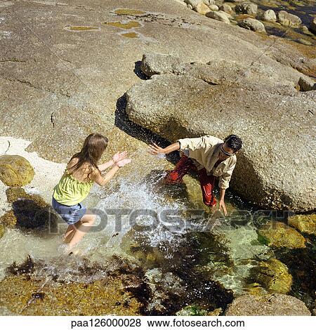 Stock Photo - Teenage boy and little girl splashing in water, high angle view. Fotosearch