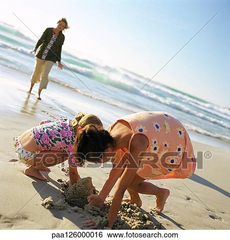 Woman walking on beach, children digging in sand View Large Photo Image Stock Photograph - Woman walking on beach, children digging in sand. Fotosearch