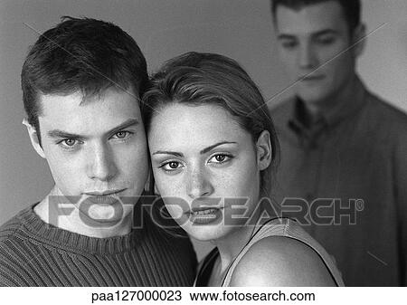 Stock Image - Man standing behind couple, portrait, b&w. Fotosearch