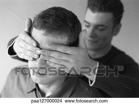 Man standing behind second man, covering his eyes, b&w View Large Photo Image Picture - Man standing behind second man, covering his eyes, b&w. Fotosearch