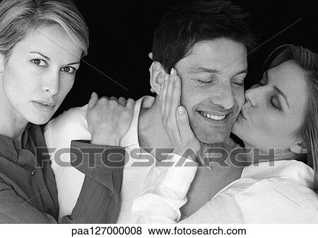 Stock Photo - Man standing between two women, being kissed by one, b&w. Fotosearch