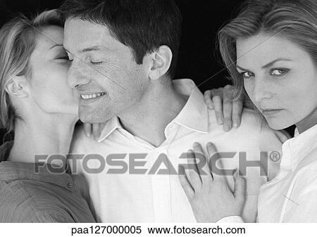 Stock Photography - Man standing between two women, being kissed by one, b&w. Fotosearch