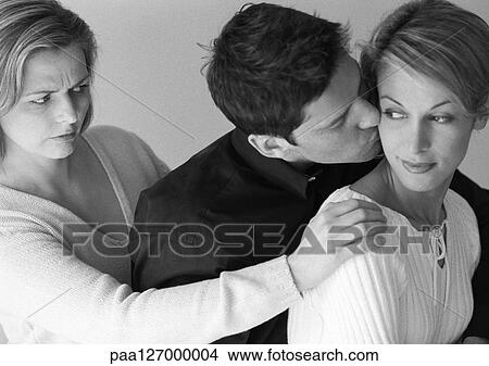 Man standing between two women, kissing one of them, b&w View Large Photo Image Picture - Man standing between two women, kissing one of them, b&w. Fotosearch
