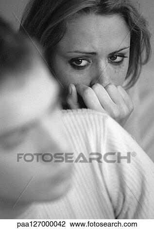 Stock Image - Tearful woman with hand against mouth, looking at man, close-up, b&w. Fotosearch