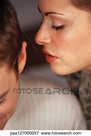 Stock Photo - Woman whispering into man's ear, close-up. Fotosearch