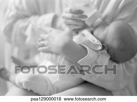 Stock Photo - Infant drinking from bottle in woman's arms, b&w. Fotosearch