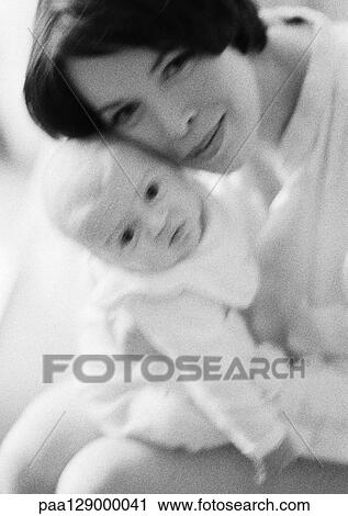 Stock Image - Mother holding infant, cheek to cheek, looking at camera, b&w. Fotosearch