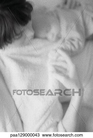 Stock Image - Mother holding sleeping infant on chest, high angle view, blurred, b&w. Fotosearch