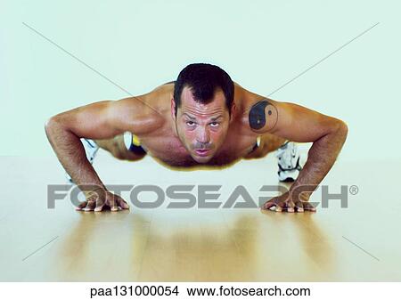 Man with tattoo doing push-ups on floor, front view View Large Photo Image Picture - Man with tattoo doing push-ups on floor, front view. Fotosearch