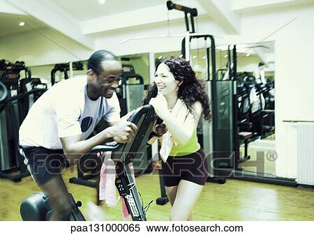 Woman standing next to man using exercise equipment in gym, laughing View Large Photo Image Stock Photography - Woman standing next to man using exercise equipment in gym, laughing. Fotosearch