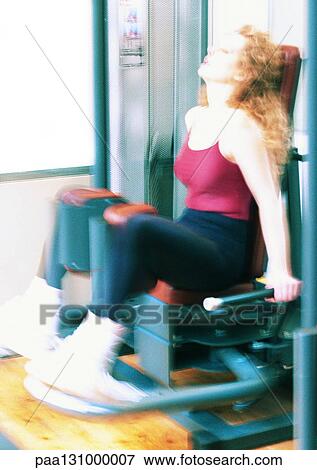 Stock Photo - Woman using weight machine in gym. Fotosearch