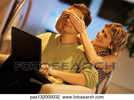 Couple, man using laptop, woman covering man's eyes from behind View Large Photo Image Stock Image - Couple, man using laptop, woman covering man's eyes from behind. Fotosearch