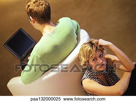 Couple sitting back to back, man on chair using laptop, woman looking up, elevated angle view. View Large Photo Image Stock Photography - Couple sitting back to back, man on chair using laptop, woman looking up, elevated angle view.. Fotosearch