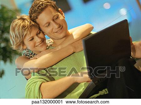 Couple smiling, man using laptop, woman with arms around man. View Large Photo Image Stock Image - Couple smiling, man using laptop, woman with arms around man.. Fotosearch