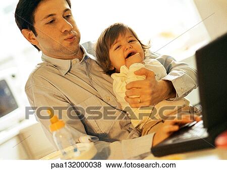 Stock Photo - Father and baby, father using laptop, baby crying.. Fotosearch