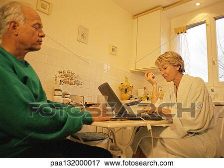 Mature couple in kitchen, woman using laptop, man holding glass View Large Photo Image Stock Photo - Mature couple in kitchen, woman using laptop, man holding glass. Fotosearch