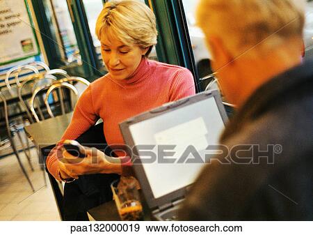 Stock Photo - Mature couple in restaurant, man using laptop, woman using cell phone.. Fotosearch