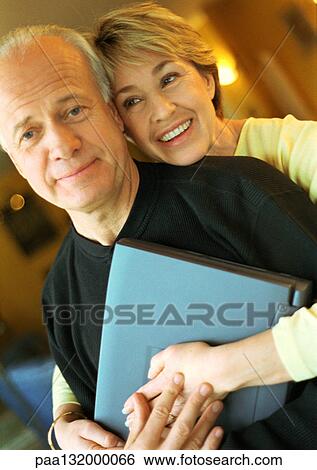 Mature couple, woman behind man with arms around him, man holding laptop, portrait. View Large Photo Image Stock Photograph - Mature couple, woman behind man with arms around him, man holding laptop, portrait.. Fotosearch