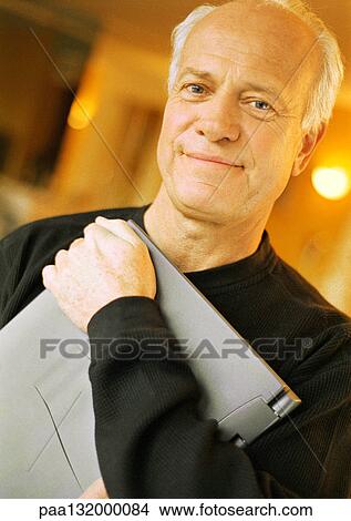 Mature man holding laptop, looking into camera, portrait. View Large Photo Image Picture - Mature man holding laptop, looking into camera, portrait.. Fotosearch