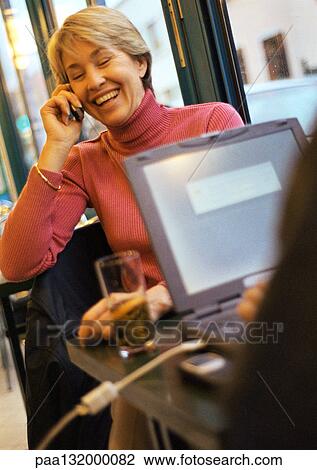 Mature woman using cell phone, sitting at table across from someone using laptop. View Large Photo Image Stock Image - Mature woman using cell phone, sitting at table across from someone using laptop.. Fotosearch
