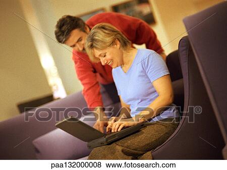 Stock Photo - Mature woman using laptop, man standing and looking over shoulder.. Fotosearch