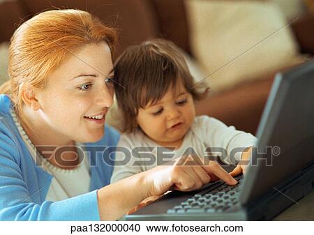 Stock Image - Mother and baby using laptop, portrait.. Fotosearch