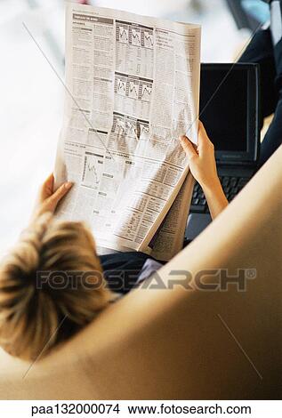 Woman reading newspaper, laptop on lap, rear view, elevated angle. View Large Photo Image Picture - Woman reading newspaper, laptop on lap, rear view, elevated angle.. Fotosearch
