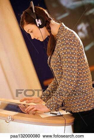 Stock Image - Young woman using computer, wearing headphones, side view.. Fotosearch