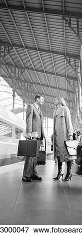 Stock Photo - Businessman and woman standing face to face on train platform, full length, b&w, vertical. Fotosearch