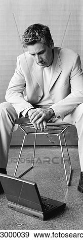 Stock Photo - Businessman sitting in chair looking down at laptop on floor, b&w, vertical. Fotosearch