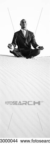 Picture - Businessman sitting in lotus position on top of dune, b&w, vertical. Fotosearch
