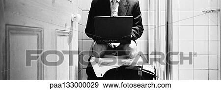 Stock Photo - Businessman sitting on toilet with pants down, using laptop, mid-section, b&w, panoramic view. Fotosearch