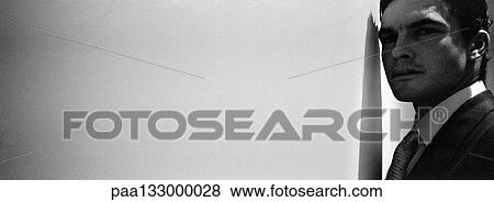 Stock Photo - Businessman standing with head close to wall, b&w, panoramic view. Fotosearch
