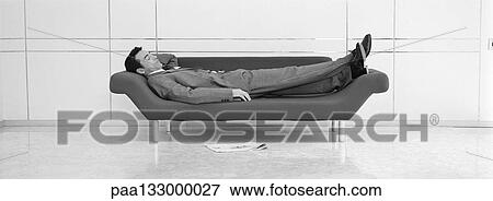 Businessman taking nap on sofa b&w, panoramic view View Large Photo Image Stock Photo - Businessman taking nap on sofa b&w, panoramic view. Fotosearch