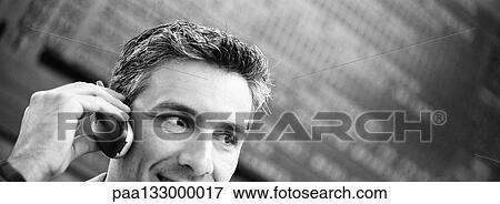 Stock Photo - Businessman talking on cell phone, departure board in background, b&w, panoramic view. Fotosearch