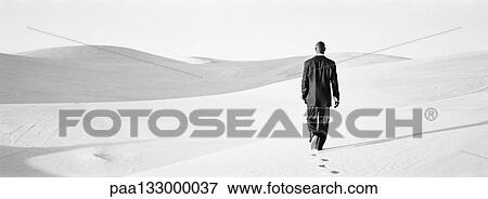 Businessman walking across dunes, rear view, b&w, panoramic view View Large Photo Image Stock Photo - Businessman walking across dunes, rear view, b&w, panoramic view. Fotosearch