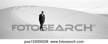 Businessman walking across ridge of dune with hands in pocket, b&w, panoramic view View Large Photo Image Stock Photo - Businessman walking across ridge of dune with hands in pocket, b&w, panoramic view. Fotosearch
